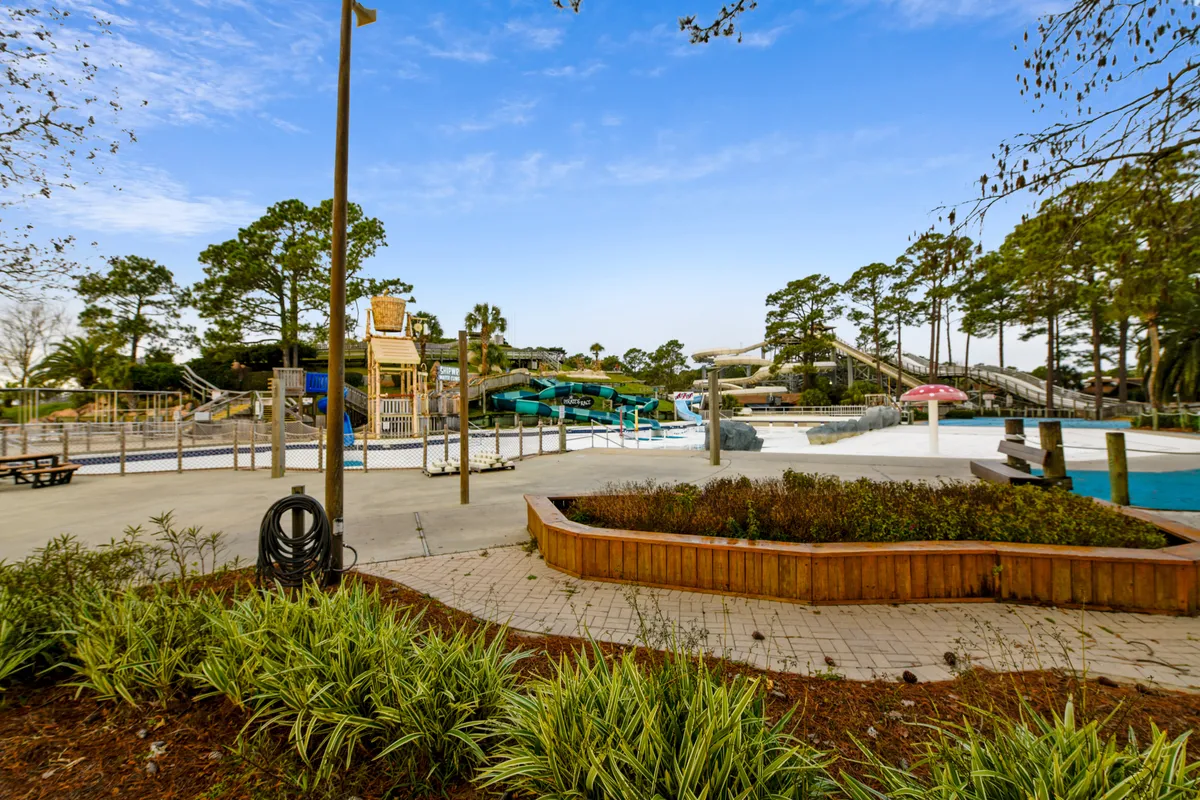 A vibrant pool scene with twisting water slides, a landscaped garden, and a spacious seating area. Children and adults are pictured enjoying the slides and relaxing by the pool, reflecting playful energy and relaxation.