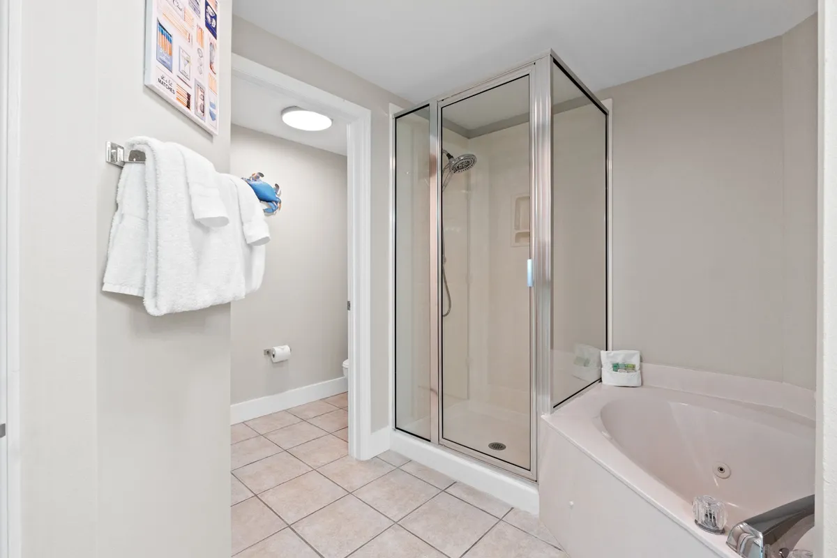 A spa-inspired bathroom showcasing a glass-enclosed shower stall, a corner Jacuzzi bathtub, neutral-toned tiled floor, and stacked white towels, creating a calm and refreshing atmosphere.
