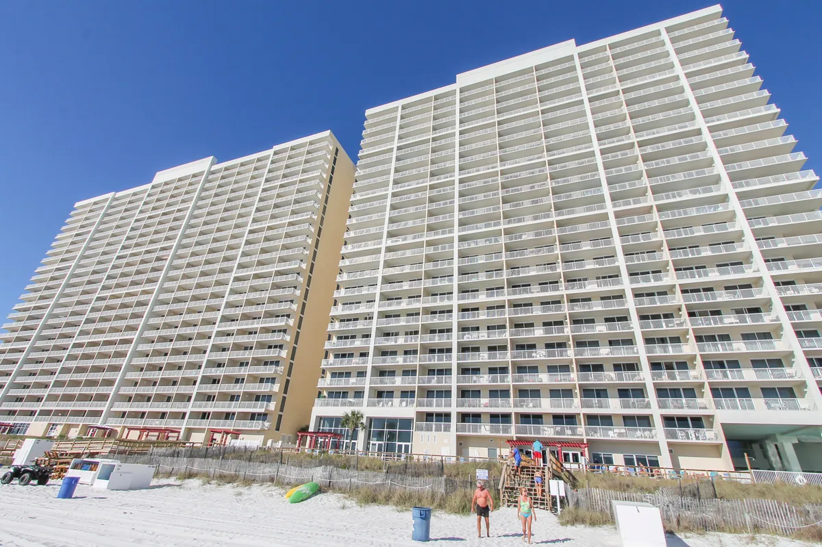 This image captures the high-rise Majestic Beach Resort buildings with private balconies overlooking the sandy beach, beachgoers enjoying the sun, and dune fencing. The ocean is visible in the background, establishing a strong sense of place and group-friendly amenities.