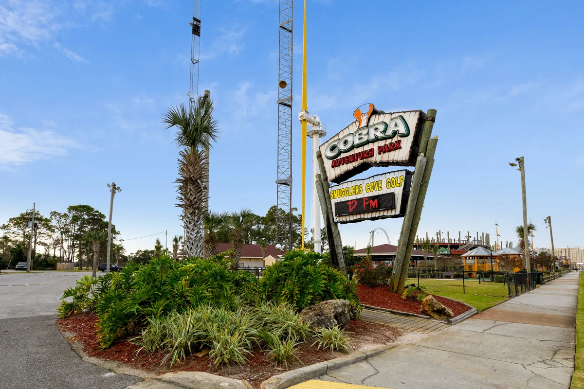 This exterior shot features the Cobra Adventure Park sign, miniature golf course area, tall amusement rides in the background, and landscaped greenery. The atmosphere is playful and energetic, ideal for families seeking excitement and variety.